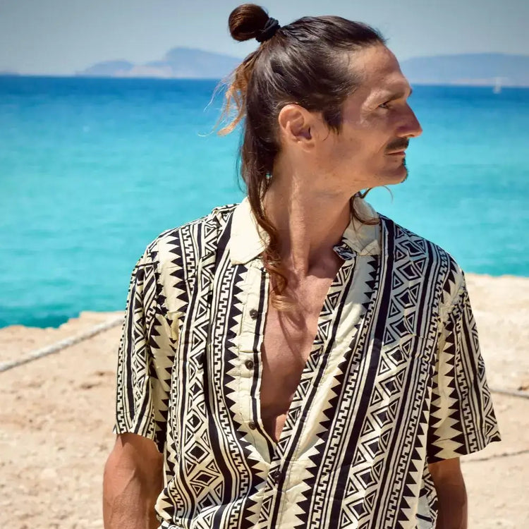 Hombre con camisa de rayón estampada mientras mira hacia el mar, ideal para un look fresco y estiloso.