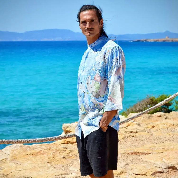 Hombre luciendo camisa rayón Aquarella de mangas 3/4 con estampado azul junto al mar.
