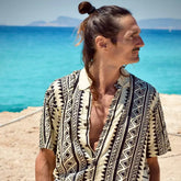 Hombre con camisa de rayón estampada mientras mira hacia el mar, ideal para un look fresco y estiloso.