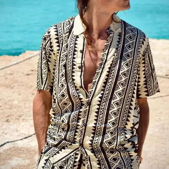 Hombre usando una camisa de rayón estampada en tonos beige y negro frente al mar, ideal para frescura y estilo.