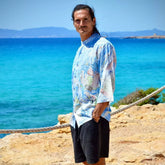Hombre luciendo camisa rayón Aquarella de mangas 3/4 con estampado azul junto al mar.