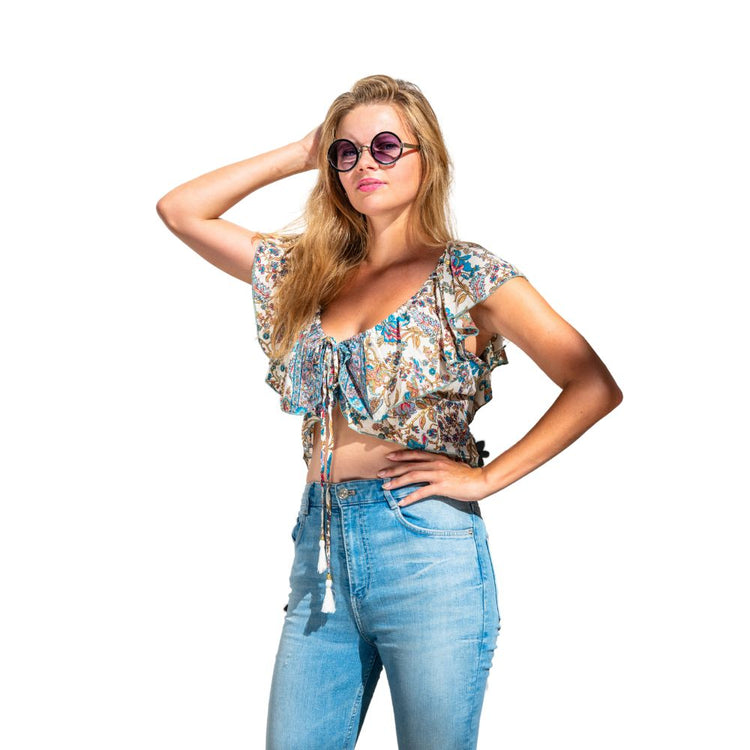 Mujer con top corto bohemio de volantes, gafas de sol y jeans claros, disfrutando del verano.
