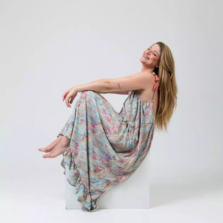 Mujer sonriente sentada en un taburete, vestida con un vestido largo bohemio Aquarella.
