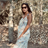 Mujer luciendo un vestido bohemio largo Aquarella, rodeada de naturaleza con un fondo de piedras y árboles.